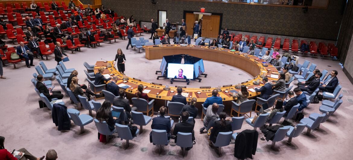 Une vue large et en contre-plongée de la salle du Conseil de sécurité des Nations unies lors d'une réunion sur le maintien de la paix et de la sécurité en Ukraine. Les délégués sont assis autour de la table en fer à cheval emblématique, avec un flux de vidéoconférence visible sur un écran au centre.