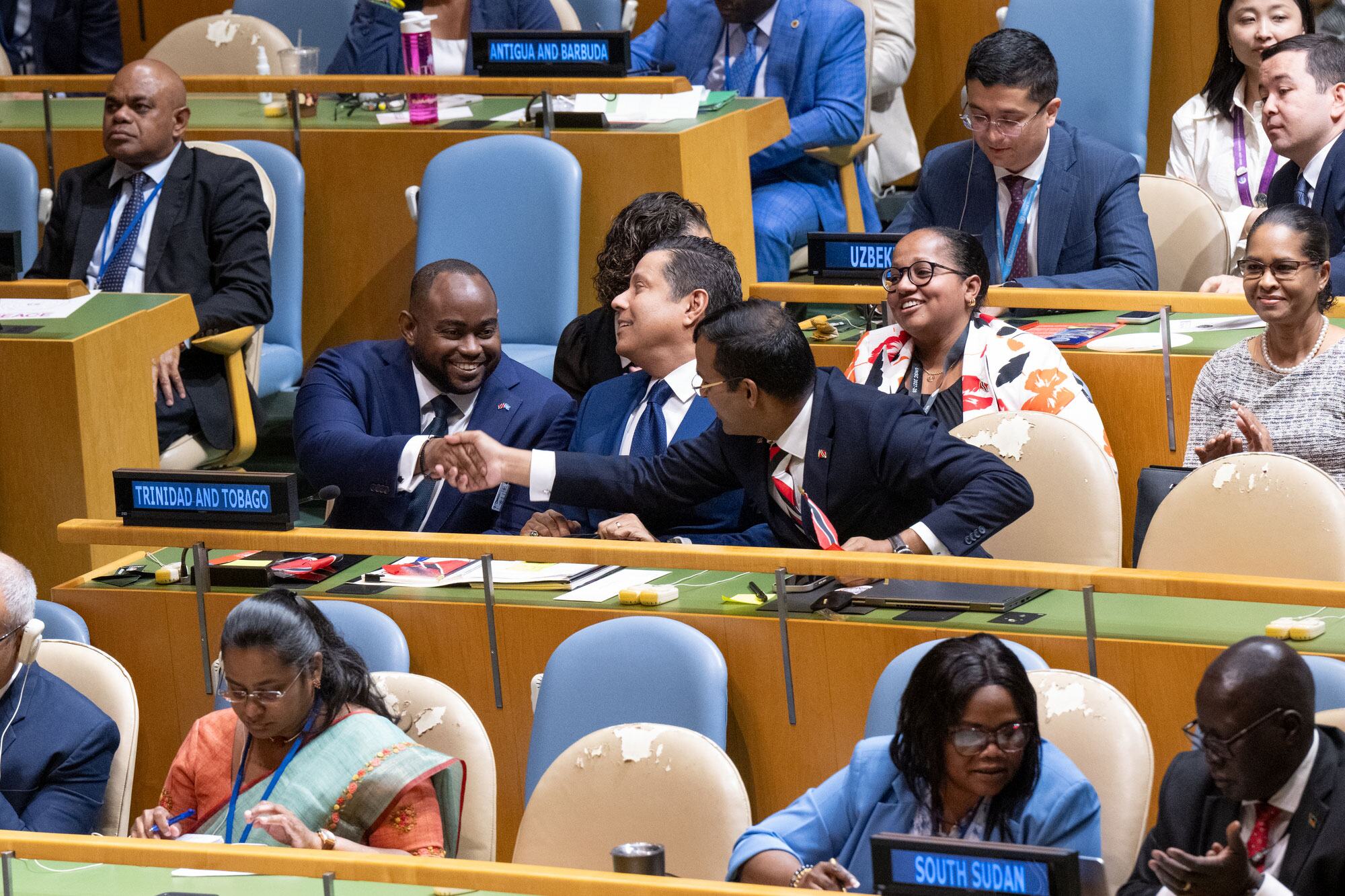 Delegates from Trinidad and Tobago celebrate a victory at a United Nations Security Council meeting, shaking hands in the chamber.