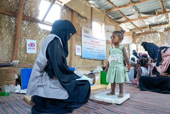 Dr. Zahra weighs 18-month-old Rana on a scale at the Al-Atira IDP camp in Lahj, Yemen, and records the data on a patient card.