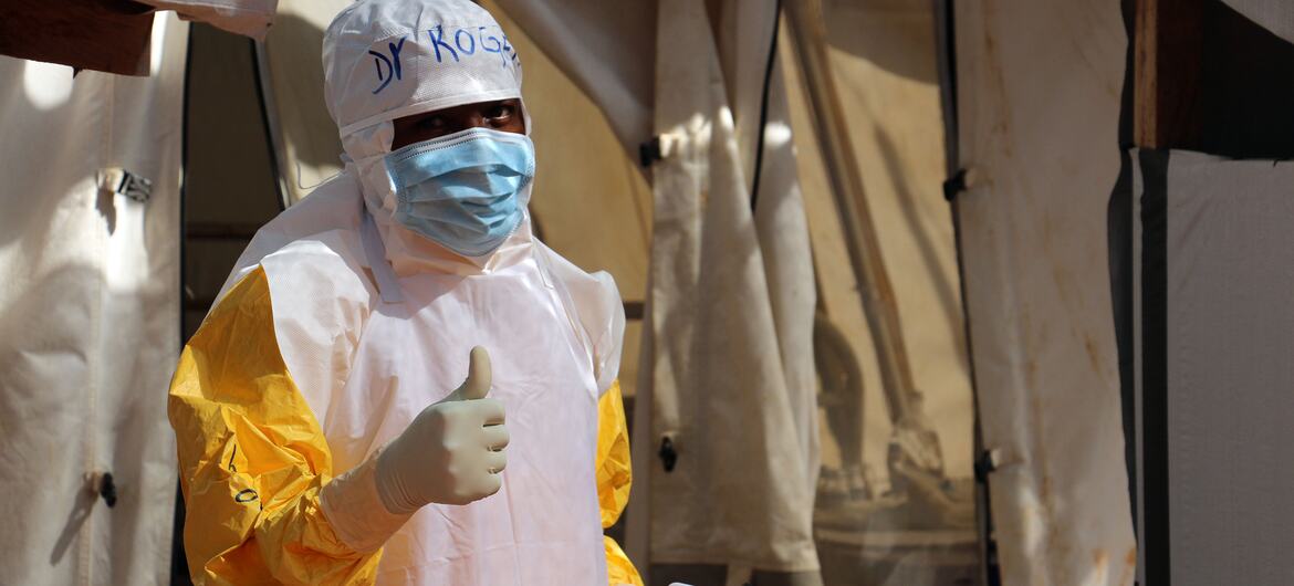 A health worker in protective gear gives a thumbs-up while holding a food kit at an Ebola treatment centre in DR Congo.