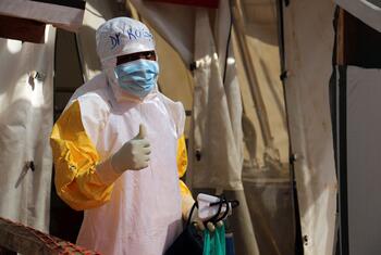 A health worker in protective gear gives a thumbs-up while holding a food kit at an Ebola treatment centre in DR Congo.