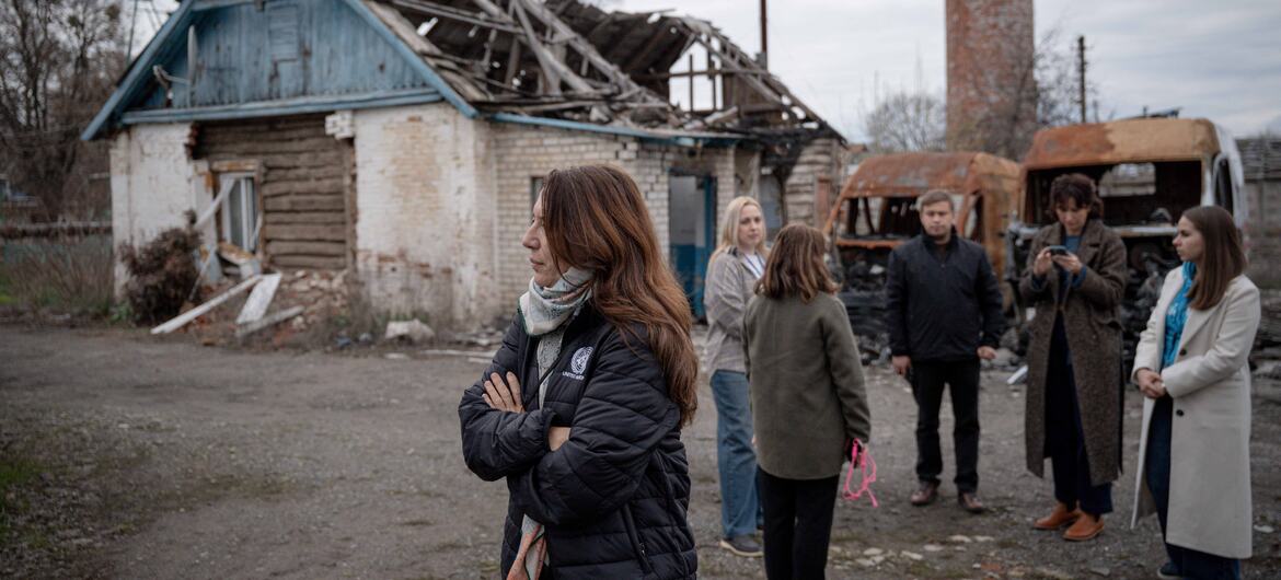 Ванесса Фрейзер из UNICEF стоит с группой людей перед разрушенным домом на Украине.