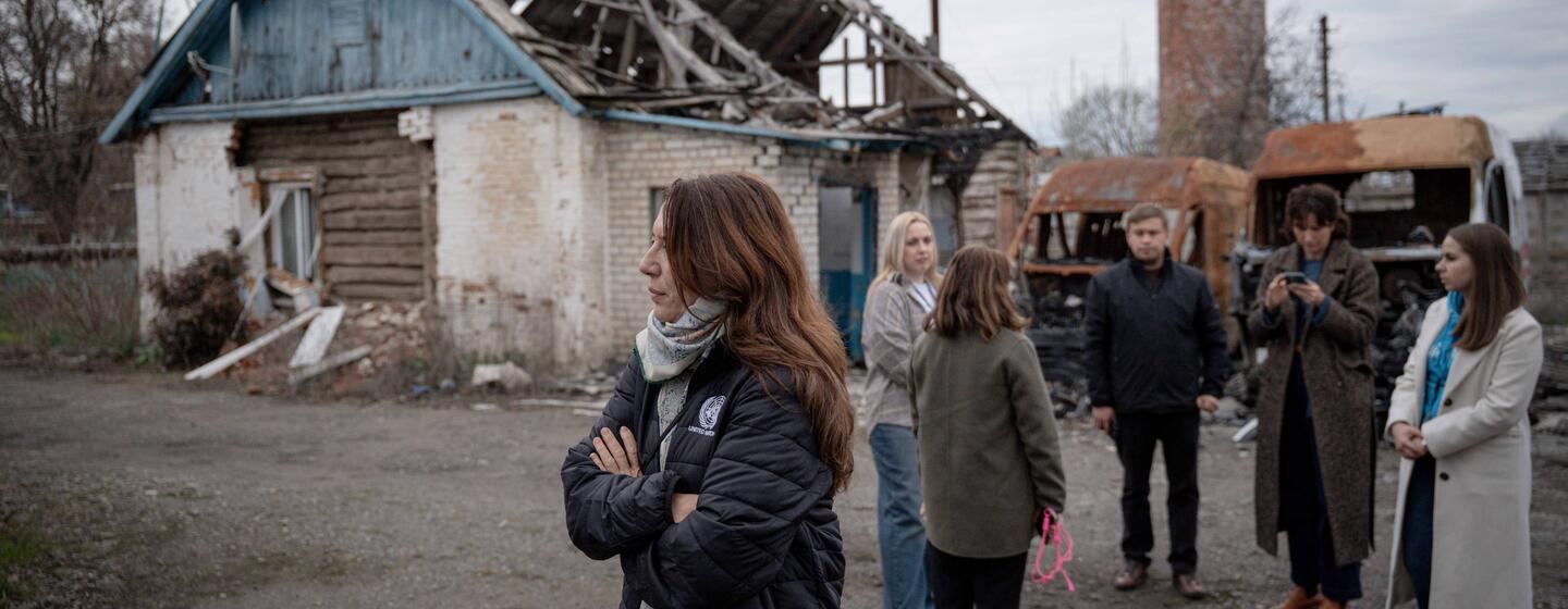 Vanessa Fraser of UNICEF stands with a group of people in front of a destroyed house in Ukraine.