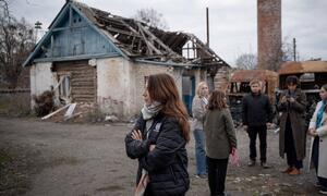 Vanessa Fraser of UNICEF stands with a group of people in front of a destroyed house in Ukraine.