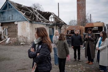 Vanessa Fraser of UNICEF stands with a group of people in front of a destroyed house in Ukraine.