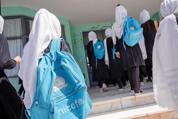 مجموعة من الطالبات يرتدين الحجاب ويحملن حقائب ظهر زرقاء تحمل شعار اليونيسف، يمشين باتجاه مبنى المدرسة.