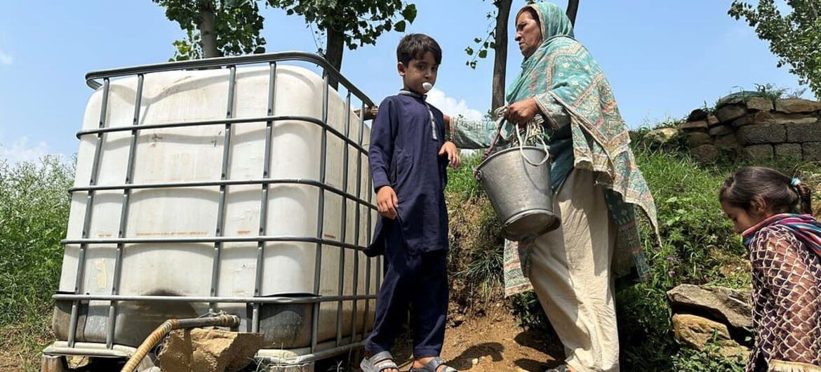 پاکستان کے پہاڑی علاقے میں، ایک خاتون بالٹی اٹھائے ہوئے ہے جب کہ ایک نوجوان لڑکا کشش ثقل سے چلنے والے پانی کے ٹینک کے تھوک سے پی رہا ہے، اس کے قریب ہی ایک اور بچہ ہے۔