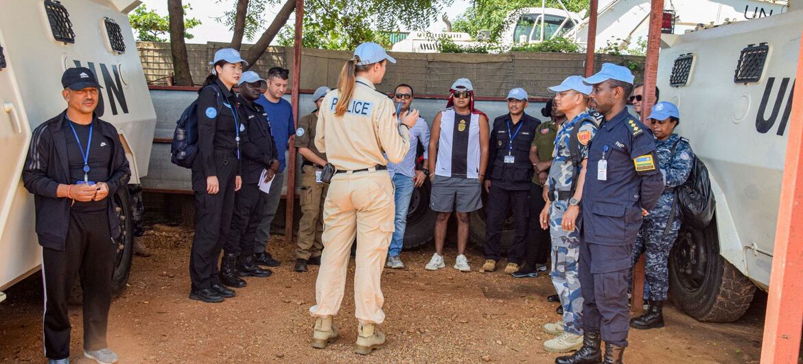 Inspector Stephanie K&ouml;nigs, a UN Woman Police Officer, addresses a group of peacekeepers and civilians near armored vehicles.