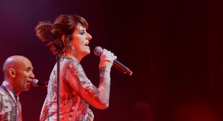 A cantora Fernanda Abreu se apresenta no palco com um microfone.  