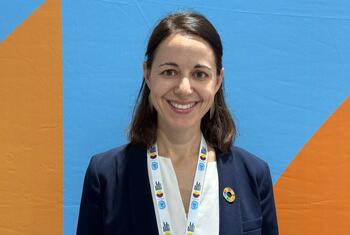 Pauline Deneufbourg pose pour un portrait lors d'un événement de ONU , arborant un cordon et une épingle sur un fond bleu et orange.