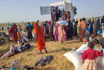 Displaced people in Sudan receive humanitarian aid from a UN truck in an open field.