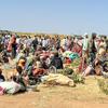 Des personnes déplacées se rassemblent dans un camp de réfugiés au Soudan, avec des travailleurs humanitaires et des véhicules des ONU visibles en arrière-plan.
