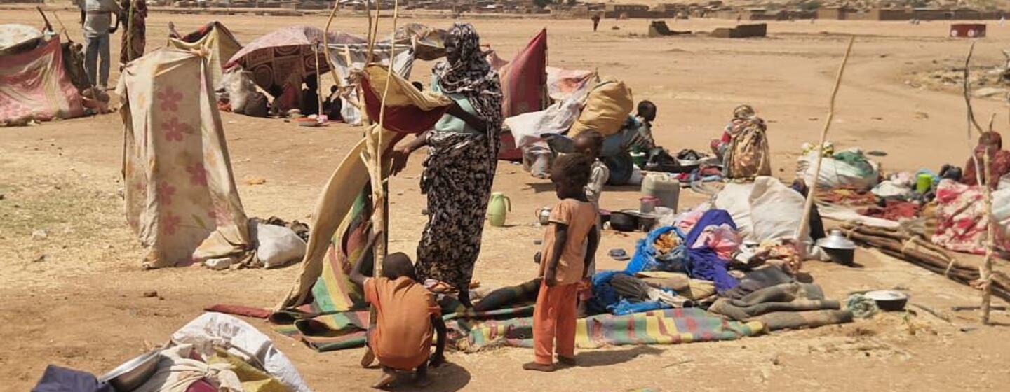 Réfugiés et personnes déplacées dans un campement de fortune au Soudan, avec des tentes de fortune et leurs effets personnels éparpillés dans un paysage aride.