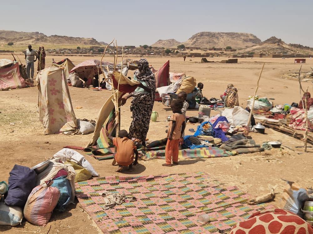 Réfugiés et personnes déplacées dans un campement de fortune au Soudan, avec des tentes de fortune et leurs effets personnels éparpillés dans un paysage aride.