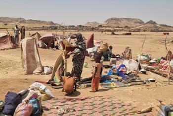 Refugees and displaced people in a makeshift settlement in Sudan, with makeshift tents and belongings spread across an arid landscape.