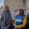 Un trabajador del PMA , vestido con un chaleco azul, conversa con una mujer local entre los escombros de un edificio destruido en Gaza.