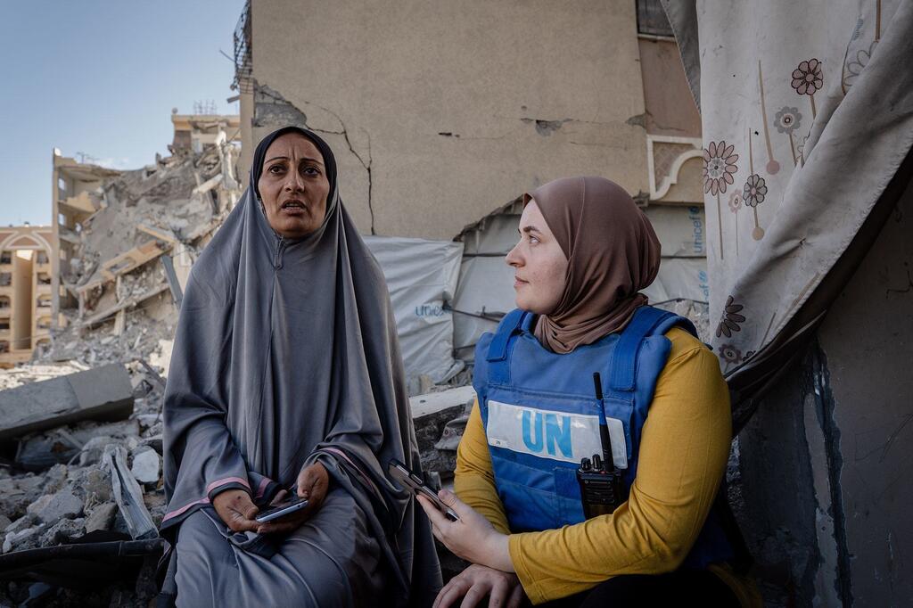 Un employé du PAM , vêtu d'un gilet bleu, discute avec une femme du coin au milieu des décombres d'un bâtiment détruit à Gaza.