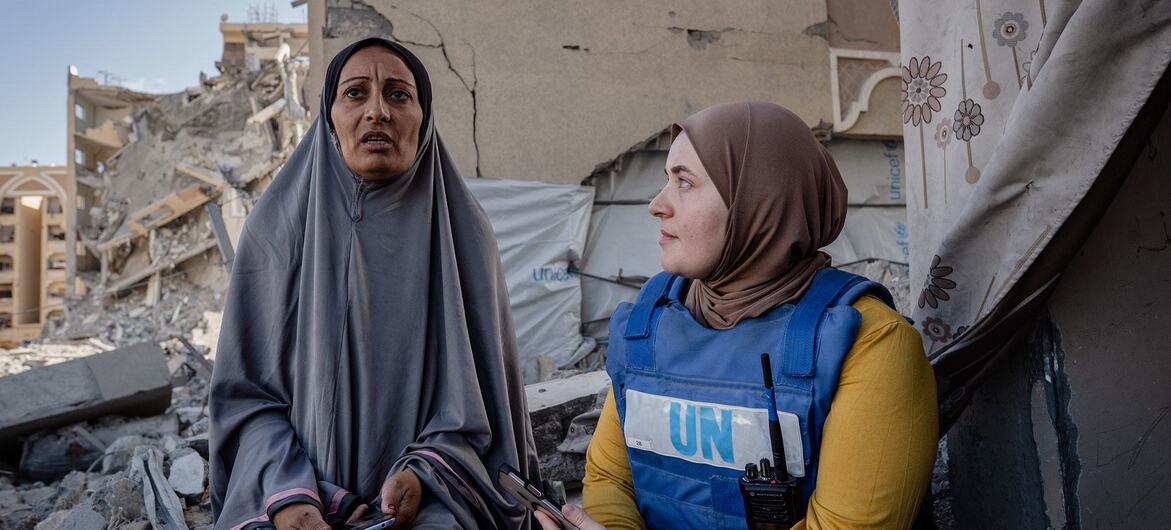 Un trabajador del PMA , vestido con un chaleco azul, conversa con una mujer local entre los escombros de un edificio destruido en Gaza.