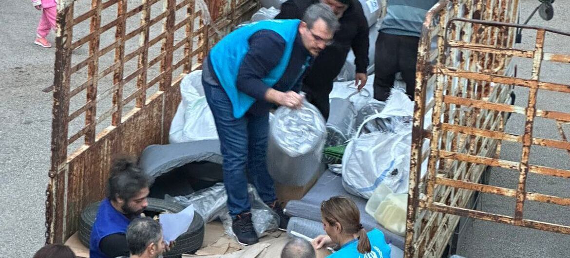Сотрудники УВКБ UNHCR раздают гуманитарную помощь, включая матрасы и одеяла, группе людей из грузовика в Ливане.