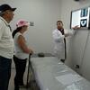 Un médico con bata blanca señala las radiografías en una pantalla mientras se las explica a un hombre y una mujer mayores en una sala de consulta.