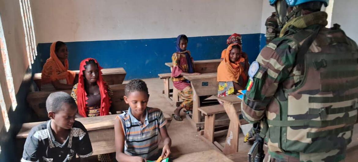 Un soldat de la paix de ONU , portant un casque bleu et un uniforme de camouflage, se tient dans une salle de classe avec des enfants.