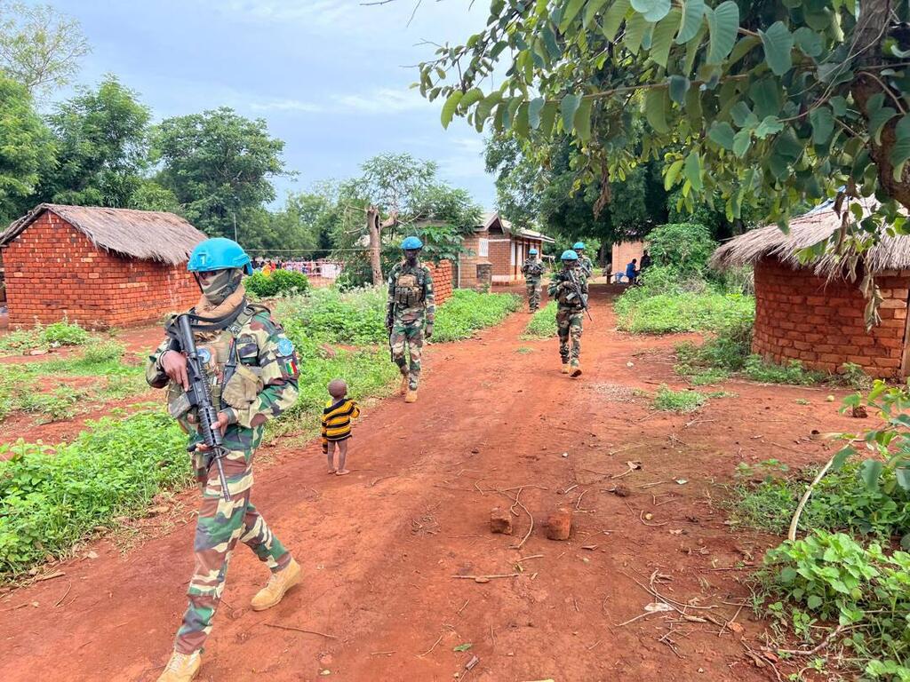 Senegalese peacekeepers from the MINUSCA Rapid Reaction Force patrol a dirt road in a rural village in the Central African Republic. A young child walks alongside the soldiers as they move through the area.