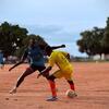 Des hommes jouent au football sur un terrain en terre battue