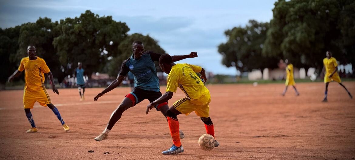 Des hommes jouent au football sur un terrain en terre battue