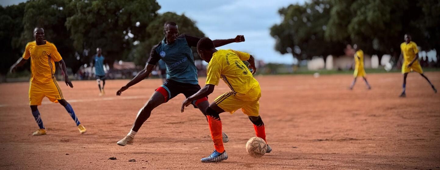 Hombres jugando al fútbol en un campo de tierra.
