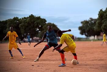 Des hommes jouent au football sur un terrain en terre battue