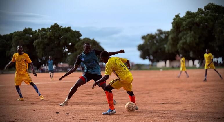Des hommes jouent au football sur un terrain en terre battue