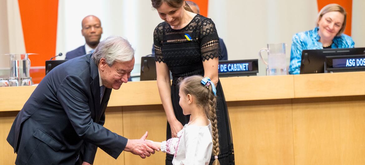 UN Secretary-General António Guterres shakes hands with a young girl at an award ceremony.