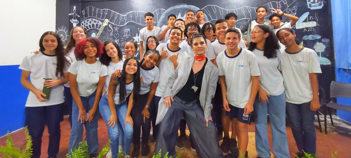A musicista Fernanda Abreu posa com um grupo de estudantes em uma sala de aula no Brasil.