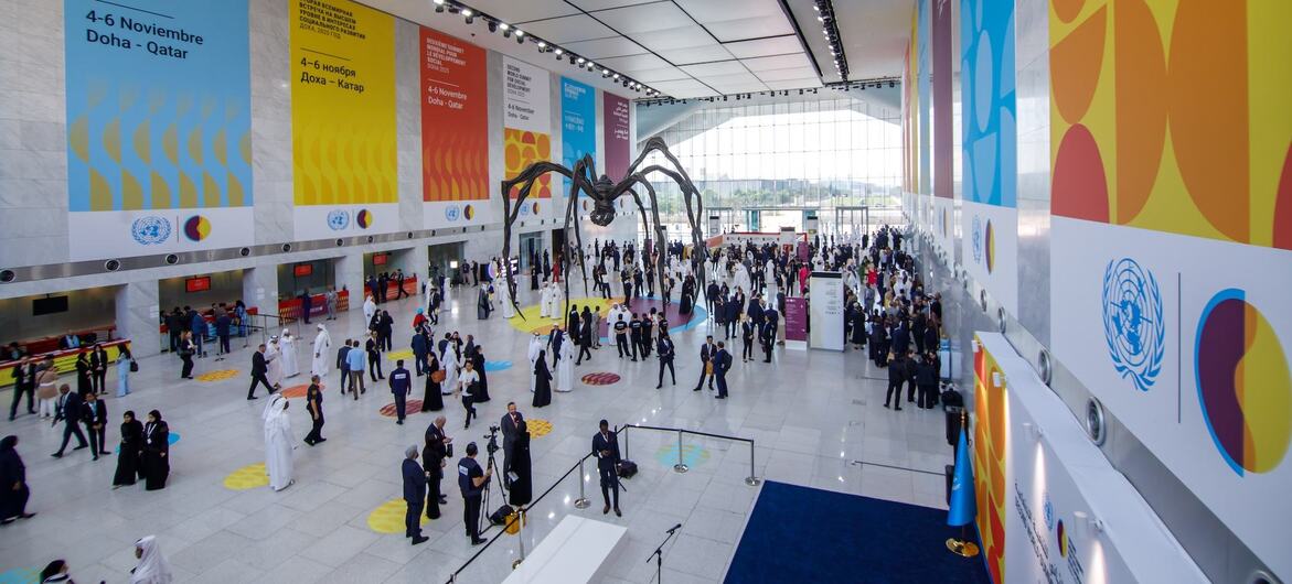 A large spider sculpture stands in a spacious conference hall during the Second World Summit on Sustainable Development in Doha, Qatar, with attendees and UN banners visible.
