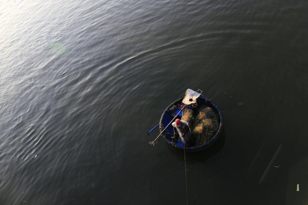 A fisherman in a traditional round basket boat on a calm river in Vietnam.