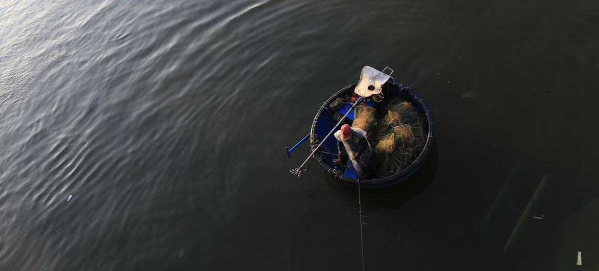 Un pêcheur dans une barque traditionnelle ronde en forme de panier sur une rivière calme au Vietnam.