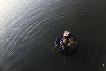 A fisherman in a traditional round basket boat on a calm river in Vietnam.
