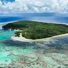 An aerial view of a tropical island in the Solomon Islands, surrounded by a vibrant turquoise coral reef and blue ocean.