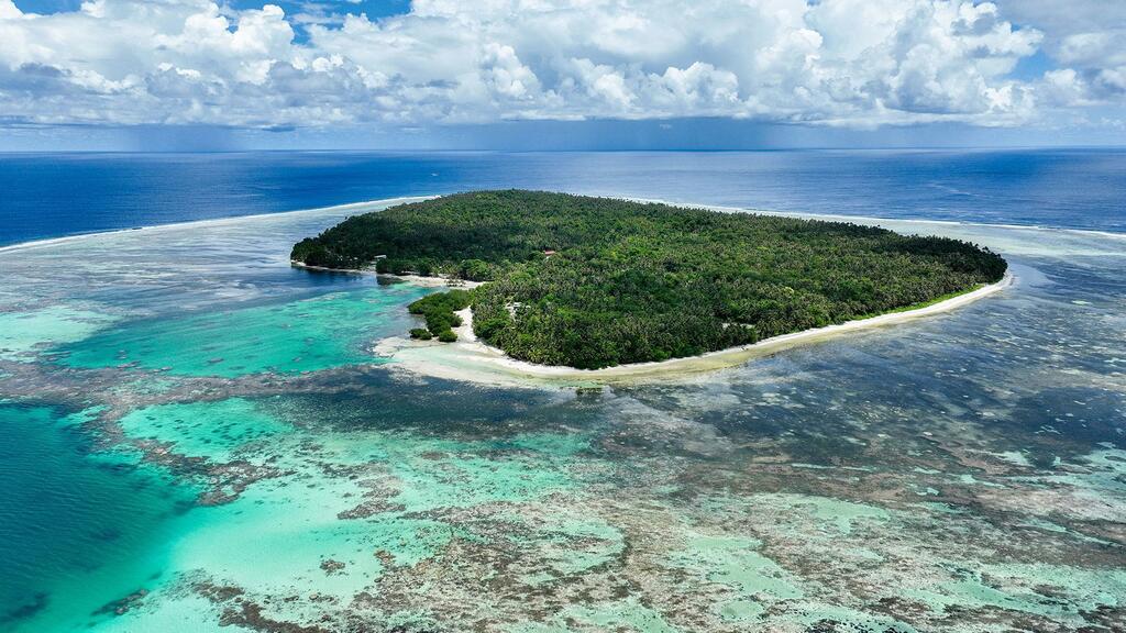 Vista aérea de una isla tropical en las Islas Salomón, rodeada por un vibrante arrecife de coral turquesa y el azul del océano.