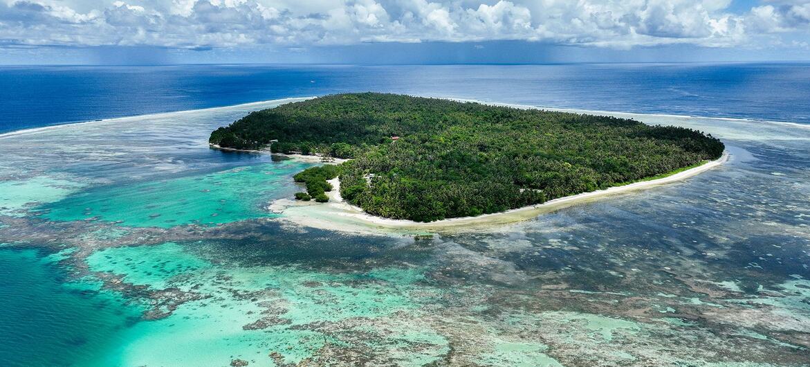An aerial view of a tropical island in the Solomon Islands, surrounded by a vibrant turquoise coral reef and blue ocean.