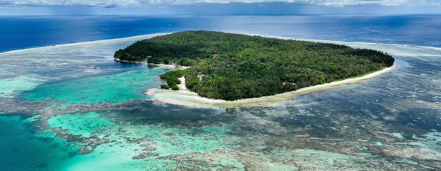 Vista aérea de una isla tropical en las Islas Salomón, rodeada por un vibrante arrecife de coral turquesa y el azul del océano.
