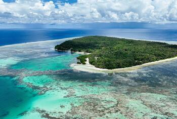 An aerial view of a tropical island in the Solomon Islands, surrounded by a vibrant turquoise coral reef and blue ocean.