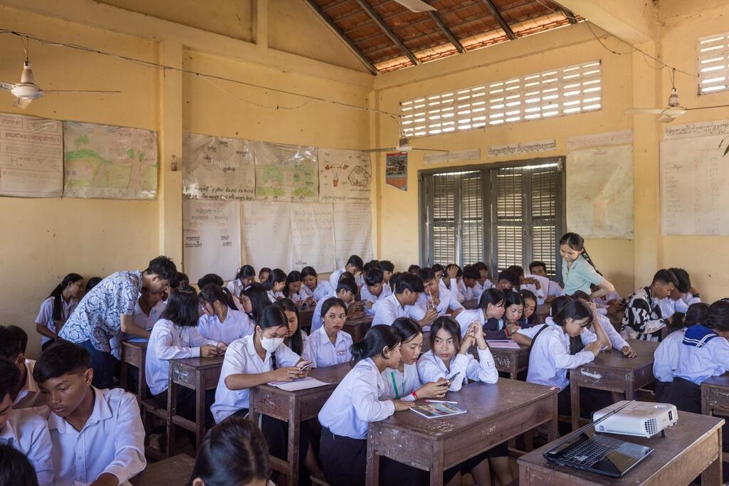 Students in a classroom setting, with a teacher assisting them.