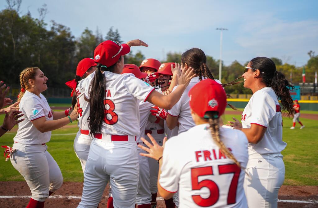 Un grupo de jugadoras de sóftbol, ​​vestidas con uniformes blancos y rojos, celebran reunidas en un círculo en un campo de béisbol.