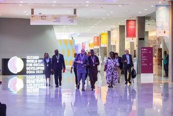 A group of attendees walks through a brightly lit conference hall at the Second World Summit on Social Development in Doha, 2025.