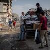 رجال وفتيان ينقلون الإمدادات الإغاثية والممتلكات على متن شاحنة عبر شارع مليء بالأنقاض والمباني المدمرة في غزة.