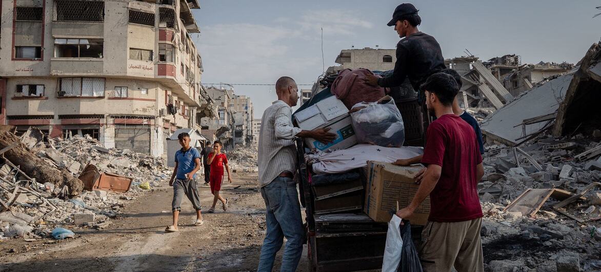 Hombres y niños transportan suministros de ayuda y pertenencias en un camión a través de una calle llena de escombros y edificios destruidos en Gaza.