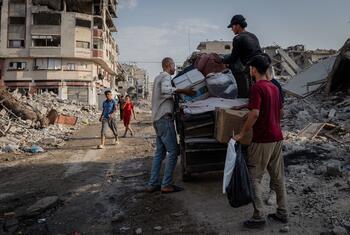 Men and boys move aid supplies and belongings on a truck through a street filled with rubble and destroyed buildings in Gaza.
