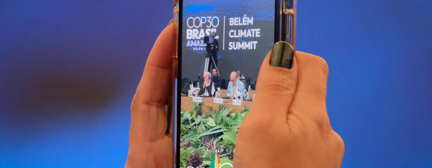 Une personne tient un smartphone affichant un écran présentant un événement du Sommet sur le climat COP30 de Belém.