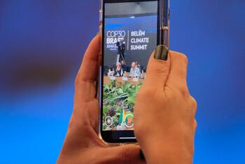 A person holds a smartphone, displaying a screen of a COP30 Belém Climate Summit event.